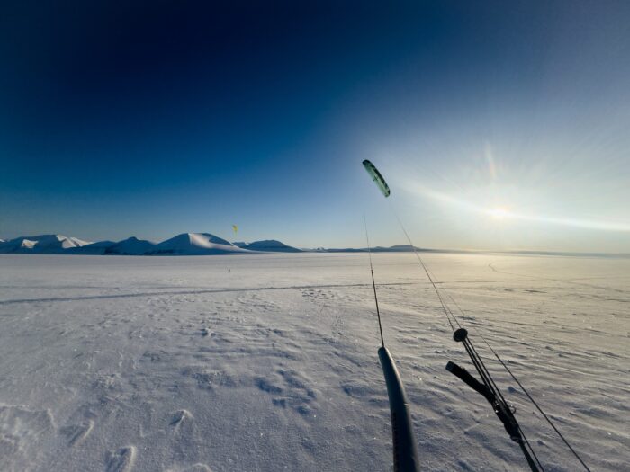 Two snowkiters travel across a snowy plateau with mountains in the distance