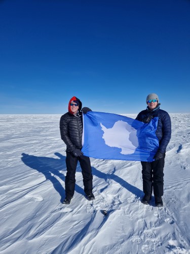 British adventurer Chris Brown standing at the Southern Pole of Inaccessibility holding a flag showing an image of Antarctica.