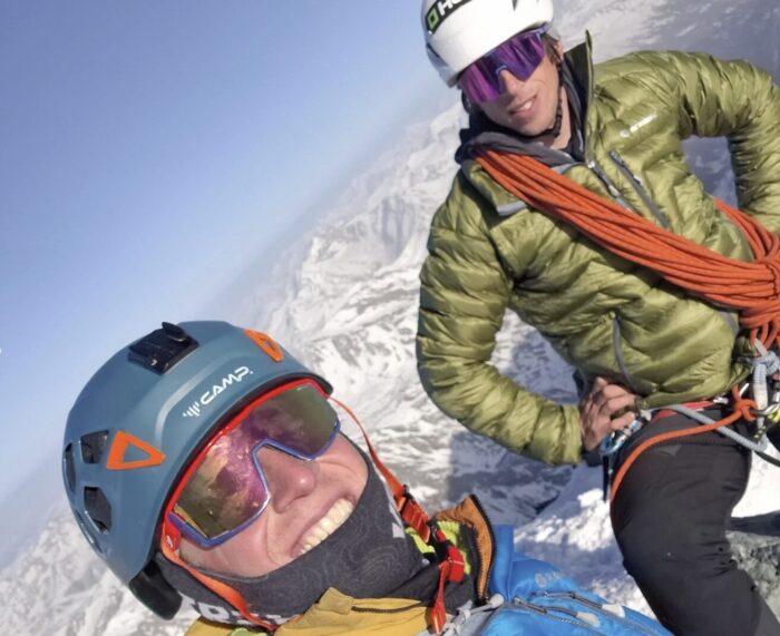 Two climbers smile on a summit in a sunny day. 