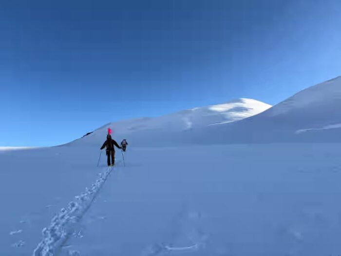A climber on a lonely, snowy mountain, with the summit far away.