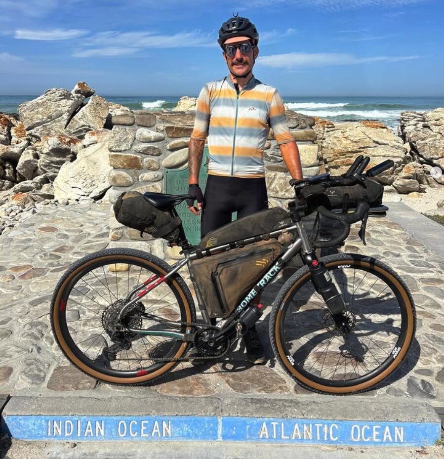 Swiss cyclist Adrien Liechti standing next to his bike at Cape Agulhas, the southernmost point in Africa