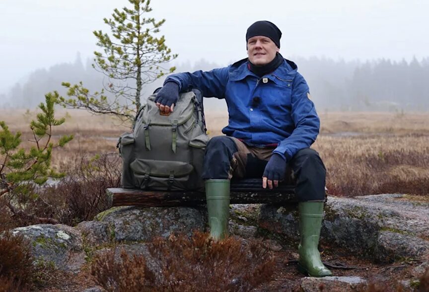 guy sitting on rock outdoors, with arm on backpack