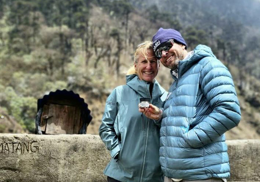 Two American climbers smile and pose with some jar of cream in an outdoor Nepal setting.
