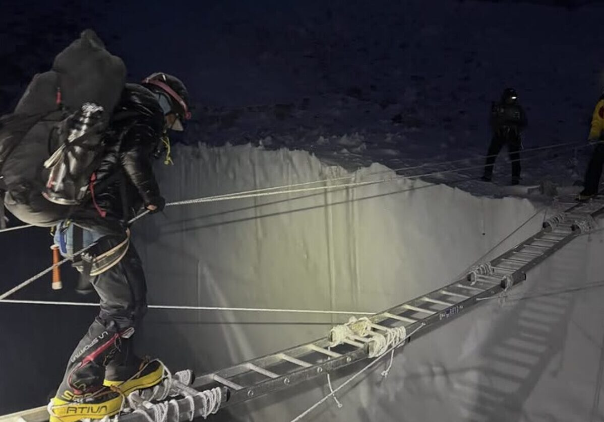 A climber in the night crossing a ladder on a crevasse.