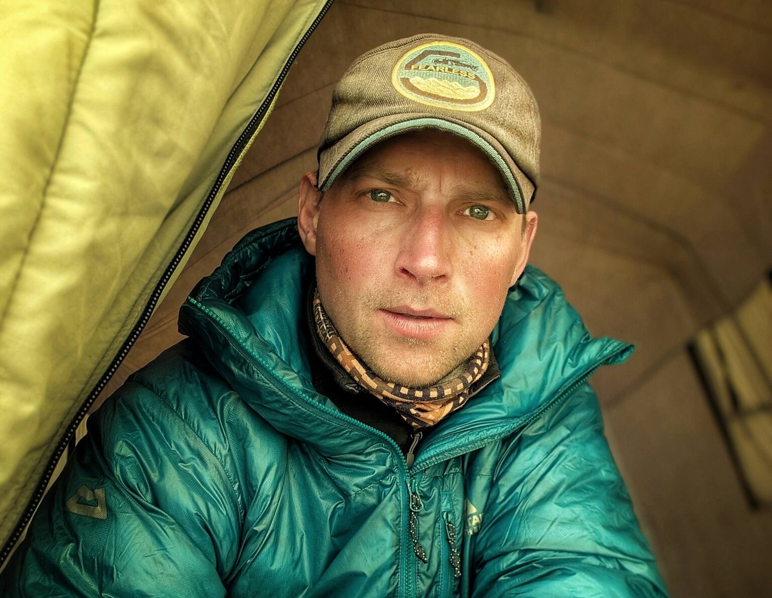 Close shot of climber saulius Damulevicius at the gate of a tent, with cap and dawn jacket.