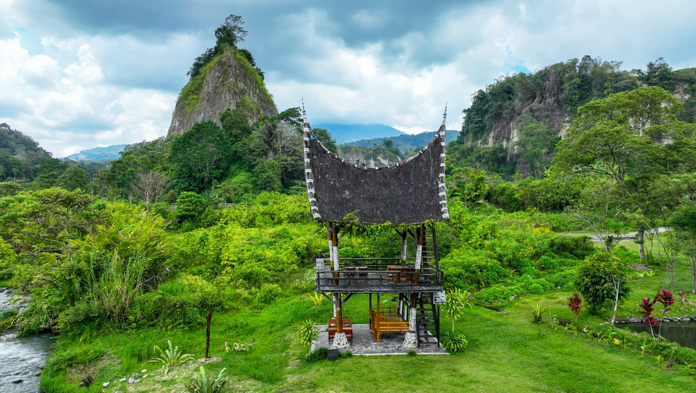 A black-roofed structure in the jungle, mountains in the distance