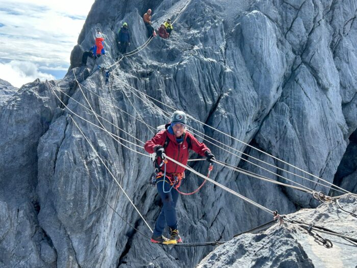 A climber negotiates a rope bridge over a chasm near the summit of Cartensz Pyramid