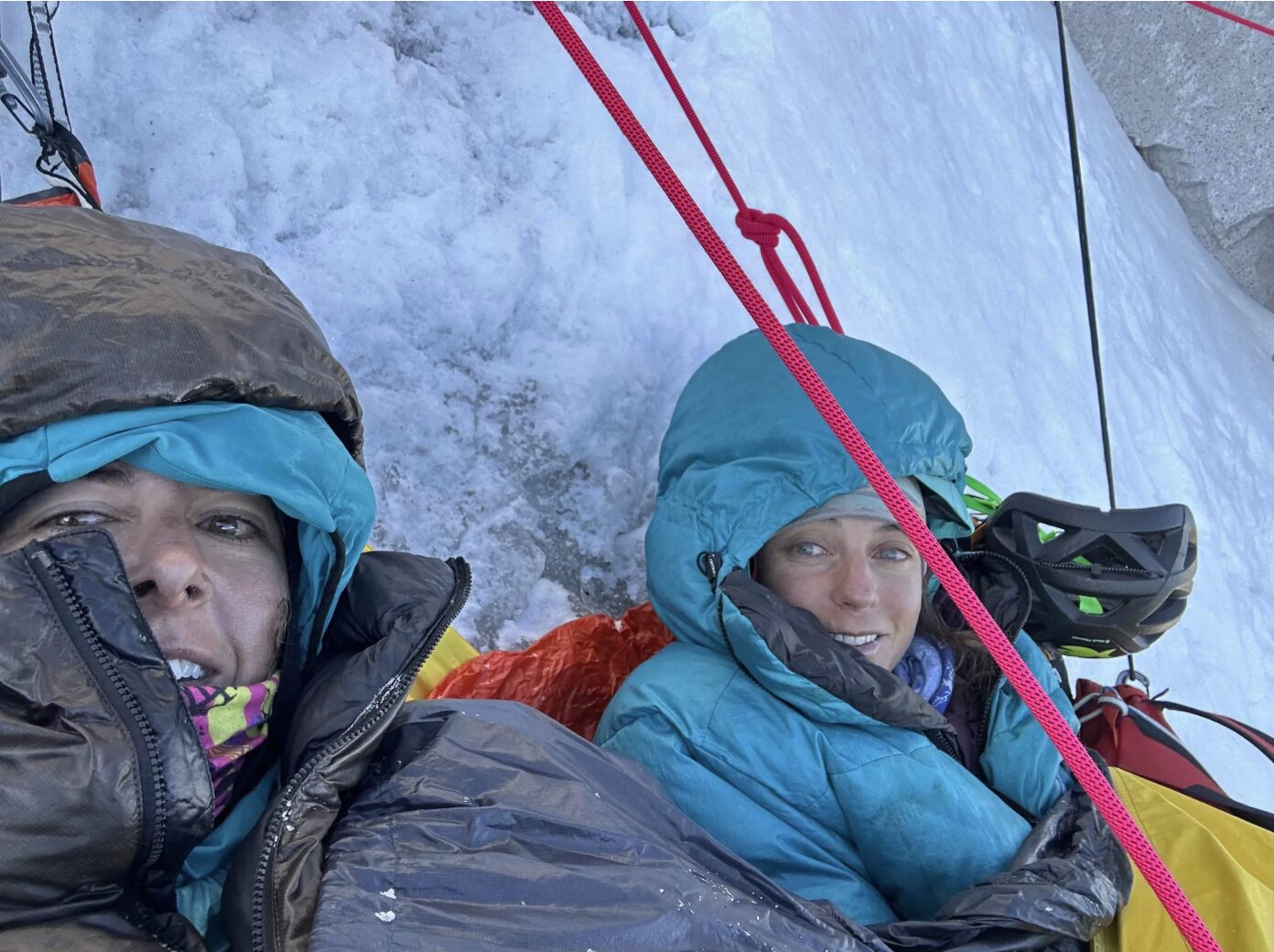 Two female climbers with jackets and hoods on, at a portaledge on an ice wall.