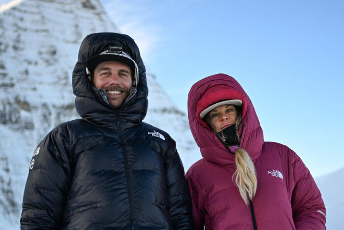Close shot of Pierrel and Lustenberg in dawn jackets with hoods on, Mt. Robson in background.