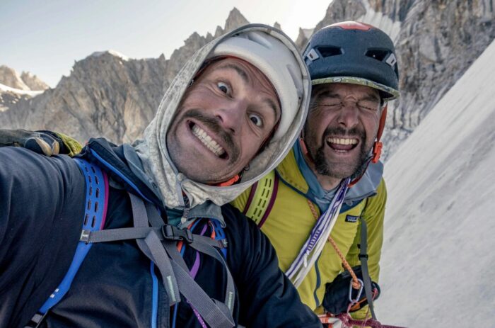 Close shot of two climbers putting funny faces with a backdrop of rocky spires and steep ice ramps.