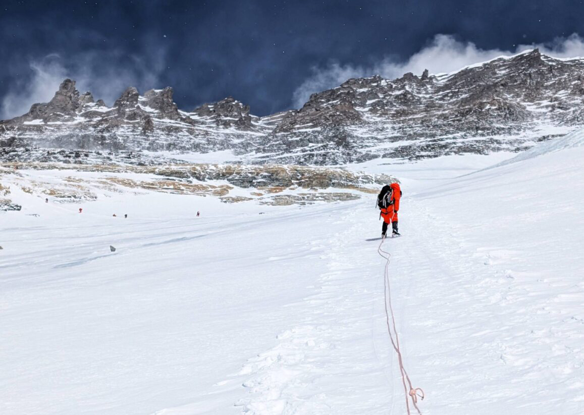 a climber on a snow slope, on fixed ropes, Lhotse summit area above him.