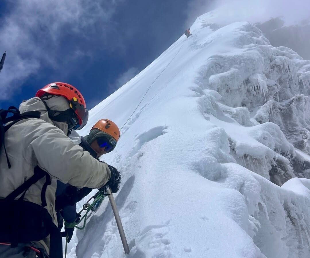Climbers on a steep snow slope holding ice axes.