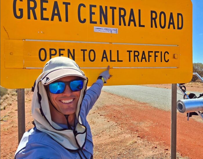 Australian adventurer Mark Gresser posing next to a road sign in the Australian outback