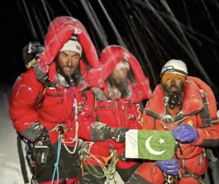 Three climbers with pakistani flags on a summit in the night under the snow.
