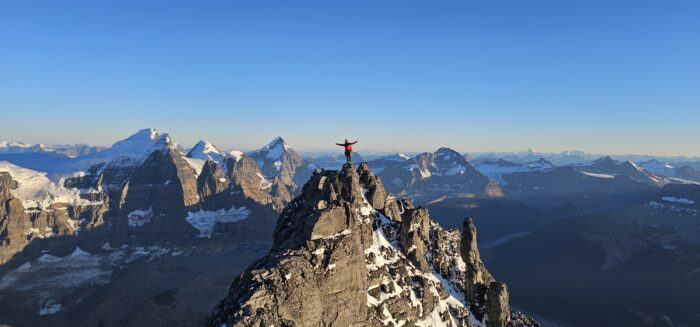 A climber on a steep rocky summit in the Canadian Rockies