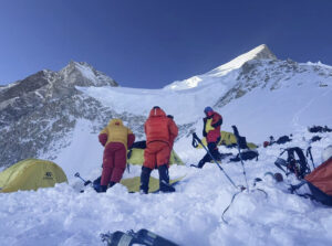 Climbers in a high camp full of fresh snow with the pyramidal summit of Gasherbrum II in background.