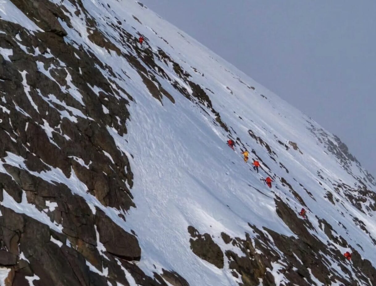 Climbers in line up a big face of rock and snow.