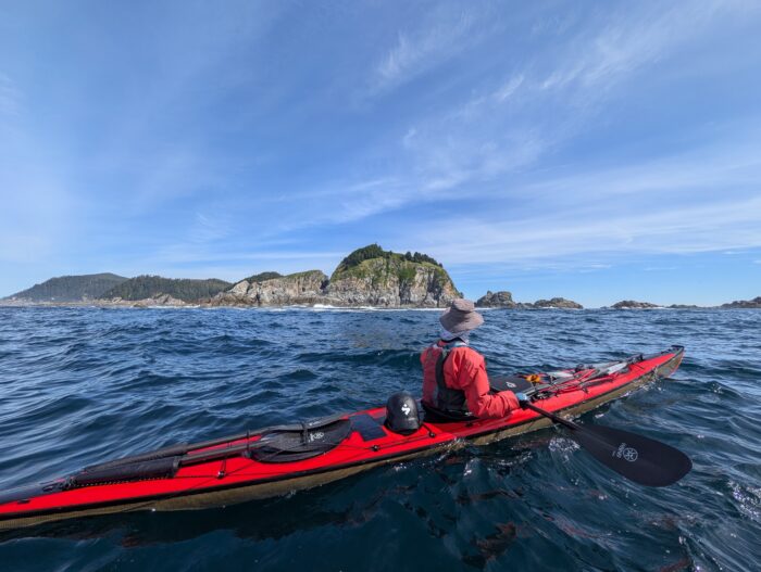 A man in a red kayak paddles past Cape St James, Moresby Island, British Columbia