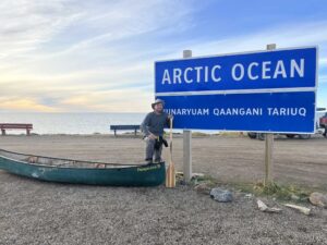 guy standing beside his canoe at Arctic Ocean sign