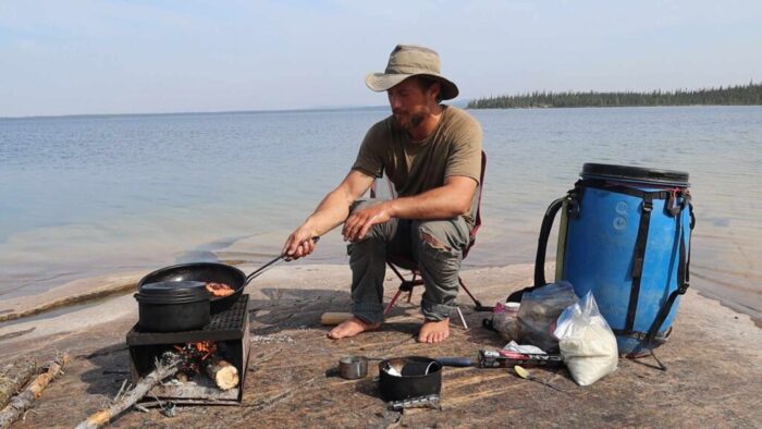 Adventurer cooking by a large lake in the north of Canada