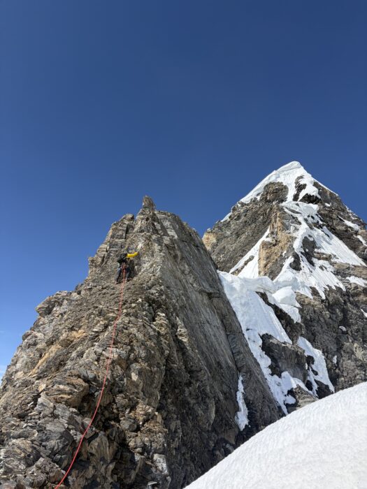 Climbers on a peak with a double summit, one on rock and another on snow.