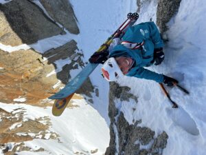 Close shot of Fay Manners on an ice wall, with ice axes and skis on her backpack.