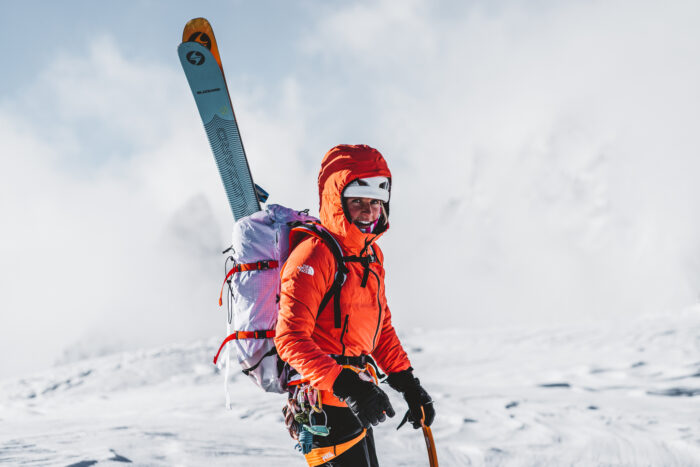 Fay Manners with skis on her back in a windy day at the Alps. 