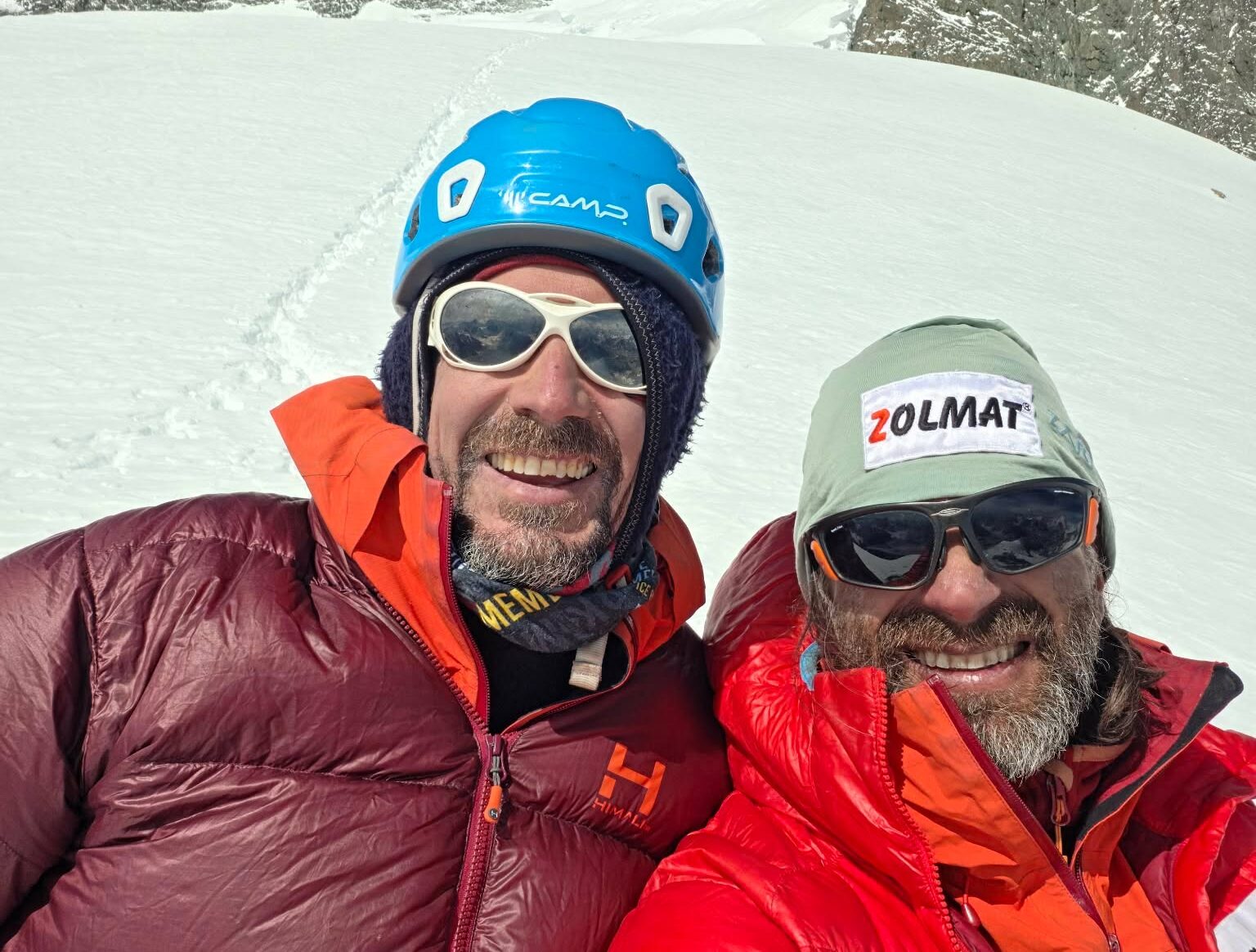Two climbers with a snow background, with helmets, sunglasses and dawn jackets.