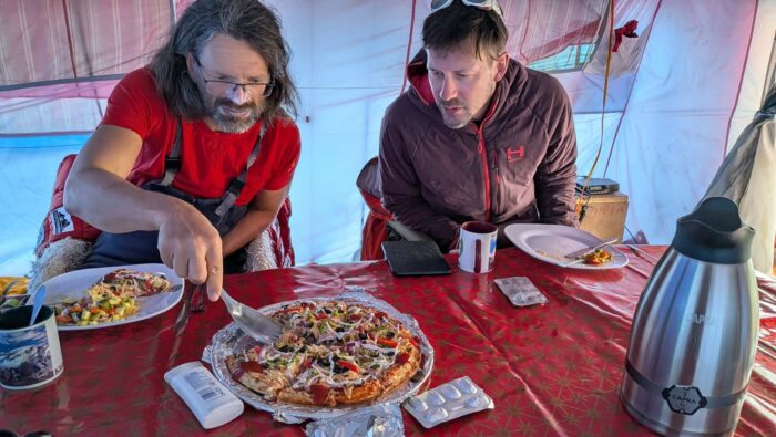 Two climbers look at a pizza in a mess tent. 