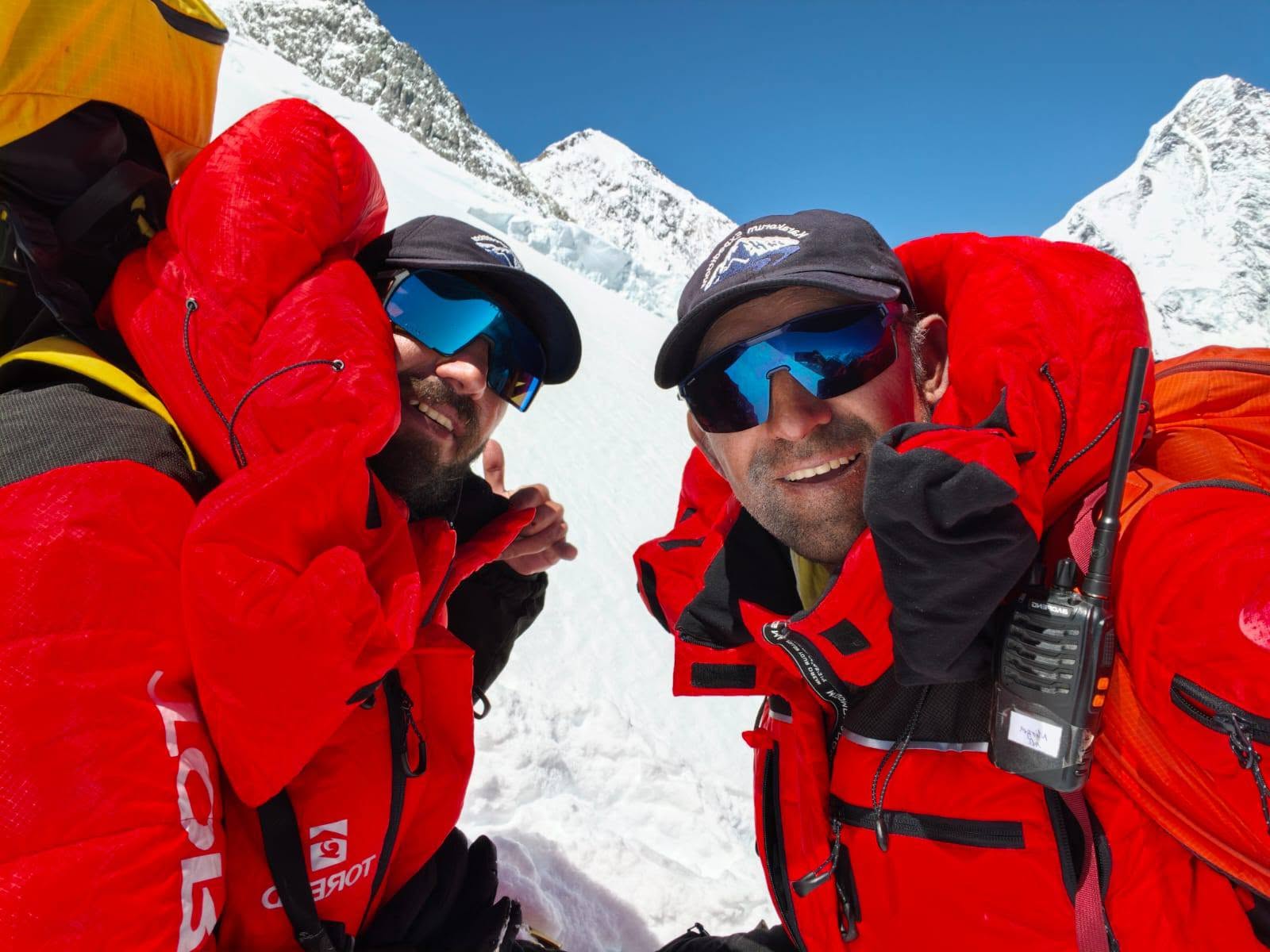 Close shots of two Pakistani climbers in bright red dawnsuits, sunglases and caps.