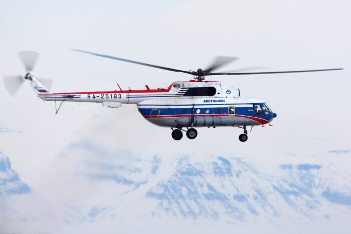 A helicopter flying past mountains in the Svalbard archipelago