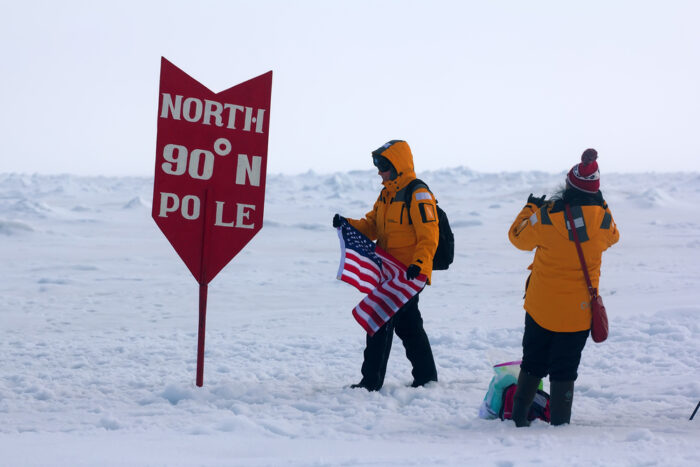 Two tourists stand next to a North Pole marker