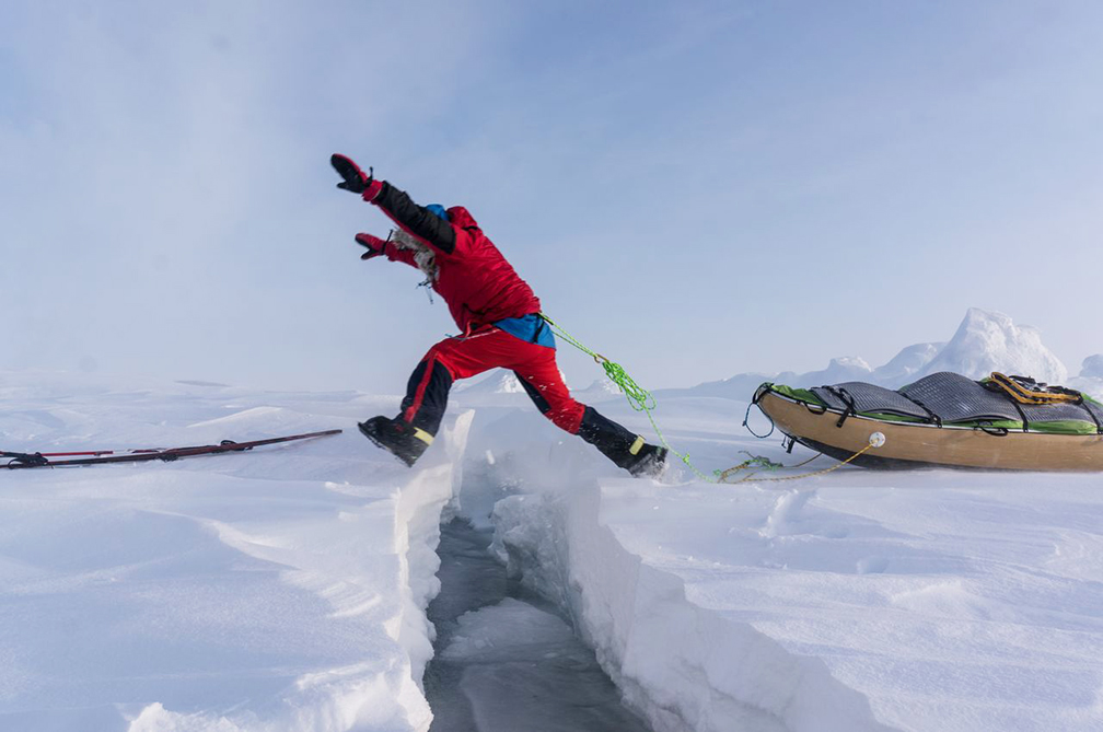 skier jumps crack in ice, with sled behind