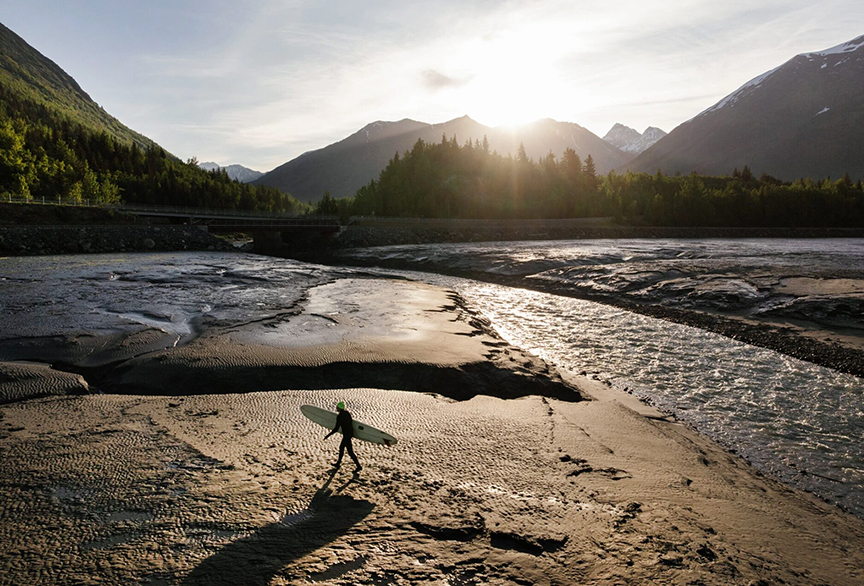 A surfer walks across the mud flats to try and catch the tidal bore wave at Turnagain Arm.
