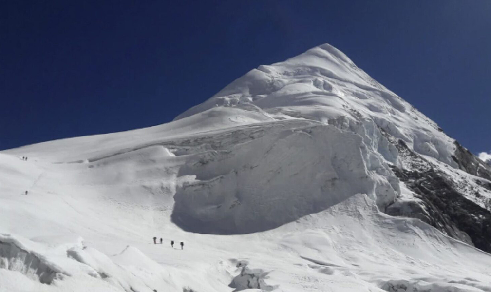 Climbers on a snowy peak, walking to the left to avoid a gib serac barrier towards a col.