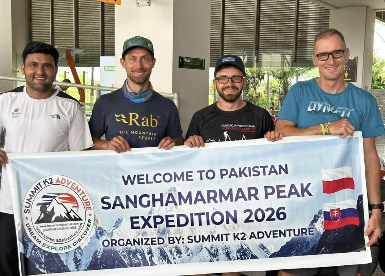 Three clibers and their local operator at an airport, holding an expedition banner.