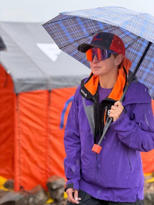 A climber with an umbrella with a tent behind her.