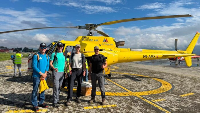 Climbers posing in front of a yellow helicopter.