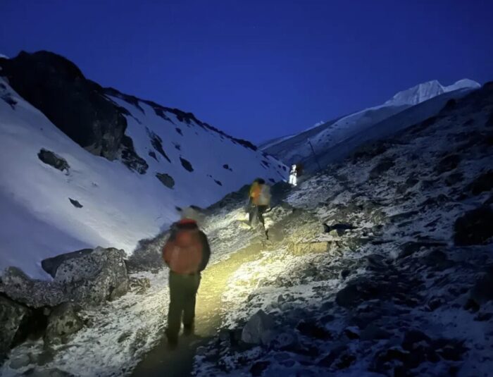 trekkers walking on scree terrain before dawn.