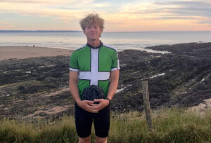 cyclist standing by coast with helmet in hand
