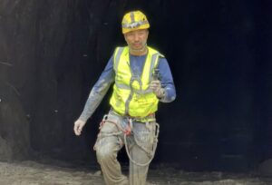 A Nepalese man with yllow helmet and vest exiting a tunnel.